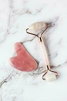 Pink jade roller and gua sha stone massager for face on white marble. photo