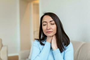 Close up of Asian woman rubbing her inflamed tonsils, tonsilitis problem, cropped. Woman with thyroid gland problem, touching her neck, girl has a sore throat photo