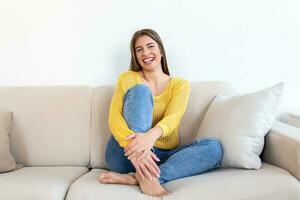 retrato de un sonriente joven mujer relajante solo en su vivo habitación sofá a hogar en el tarde foto