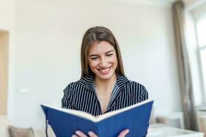 Young beautiful woman holding book, University student studying, learning language. leisure, literature and people concept - smiling woman reading book at home photo