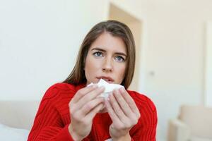 Sick desperate woman has flu. Rhinitis, cold, sickness, allergy concept. Pretty sick woman has runnning nose, rubs nose with handkerchief. Sneezing female. Brunette sneezing in a tissue photo