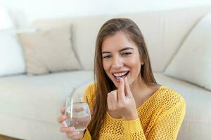 Head shot smiling young woman holding pill and glass of fresh pure water. Healthy millennial lady taking antioxidant medicine vitamins, beauty supplements for hair skin nails, healthcare concept. photo