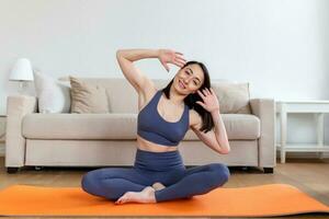 asiático atractivo sonriente mujer practicando yoga, sentado en medio loto ejercicio, ardha padmasana pose, trabajando afuera, vistiendo ropa de deporte, meditación sesión, interior lleno longitud, hogar interior foto