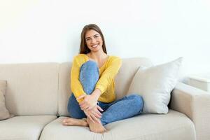 Portrait of a smiling young woman relaxing alone on her living room sofa at home in the afternoon photo