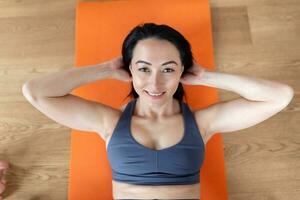 Sportswoman exercising abs doing crunches at home. healthy woman in fitness clothes in the modern living room doing abdominal crunches on fitness mat. photo