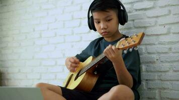 Asian boy learning to play the guitar in virtual meeting for play music online together with friend or teacher in video conference with laptop for online, Communication over Internet Learning concept