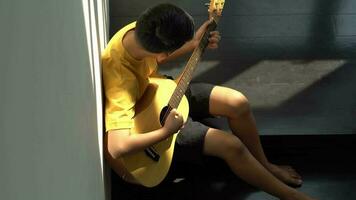 een weinig Aziatisch kind spelen en praktijk gitaar musical draad instrumenten tegen in huis, concept van musical opleiding, inspiratie, tiener kunst school- leerling. video
