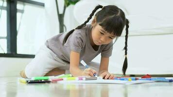 linda adorable asiático étnico niño niña participación color bolígrafo dibujo y cuadro, acostado en calentar piso, ella es teniendo divertido y risas concepto de aprender y disfrutar creativo pasatiempo, niño desarrollo. video