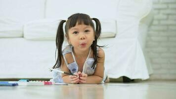 Cute adorable asian ethnic kid girl holding color pen drawing and painting, lying on warm floor, She is Having Fun and Laughs. Concept of learn and enjoy creative hobby, child development. video