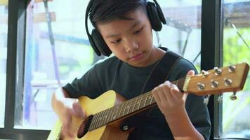 asiatischer junge, der lernt, gitarre zu spielen, in einem virtuellen treffen, um zusammen mit einem freund oder lehrer in einer videokonferenz mit einem laptop online musik zu spielen, kommunikation über das internet-lernkonzept video