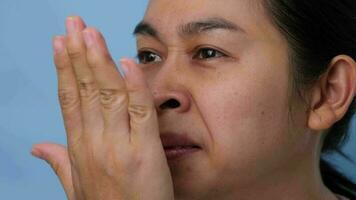 Young woman chewing gum and covering mouth to check breath with her hand on blue background. Oral health problems or dental care concept. video