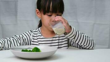 linda asiático niña Bebiendo un vaso de Leche en el Mañana antes de yendo a escuela. pequeño niña come sano vegetales y Leche para su comidas. sano comida en infancia. video