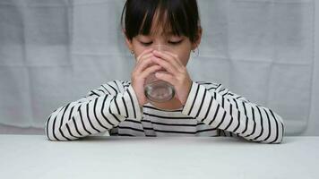 linda asiático niña Bebiendo un vaso de Leche en el Mañana antes de yendo a escuela. pequeño niña come sano vegetales y Leche para su comidas. sano comida en infancia. video
