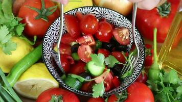 avec deux fourches il mélanges le salade avec beaucoup de tomates sur le assiette parmi le légumes, épices et huiles sont mixte donc cette elles ou ils sont uniformément distribué video