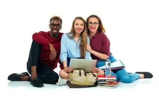 Three students sitting with books, laptop and bags isolated on white background photo