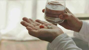 homme mains détient une bleu capsule et verre de l'eau plus de le tableau, prêt à prendre médicaments. malade homme avoir besoin médicament de mal de crâne et froid, anti douleur, nutritionnel supplément. santé se soucier concept. video