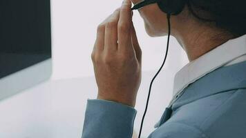 Call center agent with headset working on support hotline in modern office with copy space. Portrait of mature positive agent in conversation with customer over headset looking at camera. video