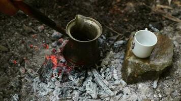 Turkish coffee cooked on red ember coal and the image of the cup on the stone next to it, an image of coffee cooked in a natural environment video