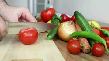 un' uomo chopping pomodori a partire dal verdure in piedi su il tavolo mette il tritato pomodori su il piatto per cucinare video