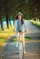 encantador joven mujer en un sombrero montando un bicicleta en un parque foto