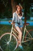 encantador joven mujer en un sombrero con un bicicleta en un parque foto