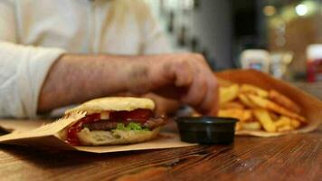 un hombre inmersión papas fritas en el salsa desde un hamburguesa menú acostado en el mesa, comiendo rápido comida es perjudicial a salud video