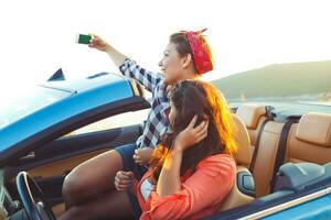 Two young beautiful girls are doing selfie in a convertible photo