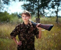 Young beautiful girl with a shotgun looks into the distance photo