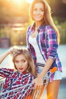 Two happy beautiful teen girls driving shopping cart outdoors photo