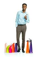 contento africano americano hombre con compras pantalones y participación crédito tarjeta en blanco antecedentes foto