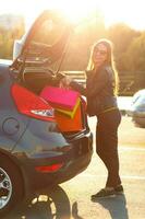 caucásico mujer poniendo su compras pantalones dentro el coche maletero foto