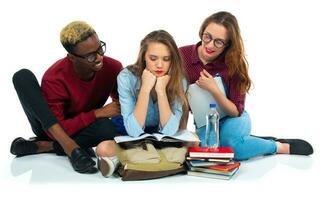 Three students sitting with books, laptop and bags isolated on white background photo