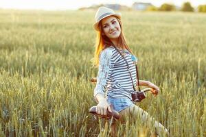 encantador joven mujer soportes en un campo con su bicicleta foto