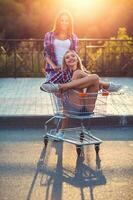 Two happy beautiful teen girls driving shopping cart outdoors photo