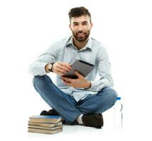 Young bearded smiling man holding a tablet with books and a bottle of water sitting on a white photo