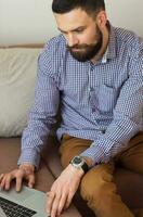 Young bearded man working on laptop at home photo