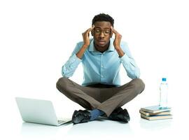 Happy african american college student in stress sitting with laptop, books and bottle of water on white photo
