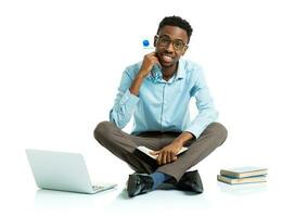 Happy african american college student with laptop, books and bottle of water sitting on white photo