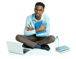 african american college student with laptop, books and bottle of water sitting on white photo