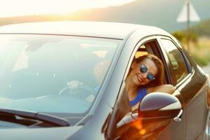 sonriente mujer conducción un coche a puesta de sol foto