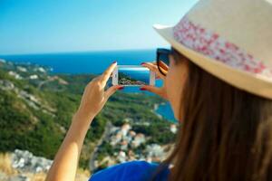 niña en sombrero haciendo fotos de el adriático mar por el teléfono inteligente