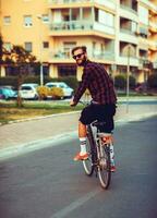 elegante hombre en Gafas de sol montando un bicicleta en ciudad calle foto