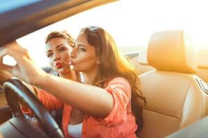 dos joven hermosa muchachas son haciendo selfie en un convertible foto