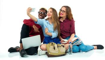 Happy students with books, laptop,  bags and makes selfie on white background photo