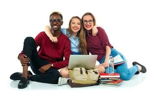 Three students sitting with books, laptop and bags isolated on white background photo