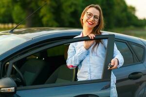 joven mujer en pie cerca un coche con llaves en mano foto