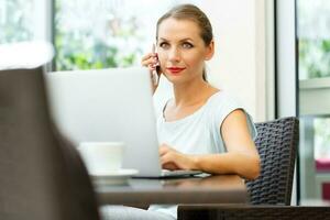 Young woman sitting in a cafe with a laptop and talking on the cell phone photo