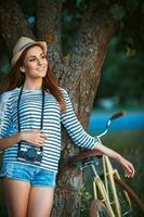 encantador joven mujer en un sombrero con un bicicleta en un parque foto