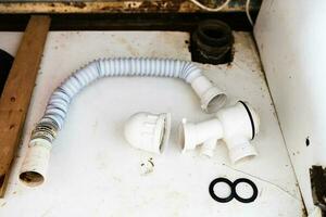 disassembled old plastic siphon next to sewer pipe photo