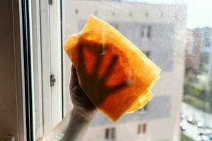 mano toallitas sucio ventana en de muchos pisos ciudad casa foto